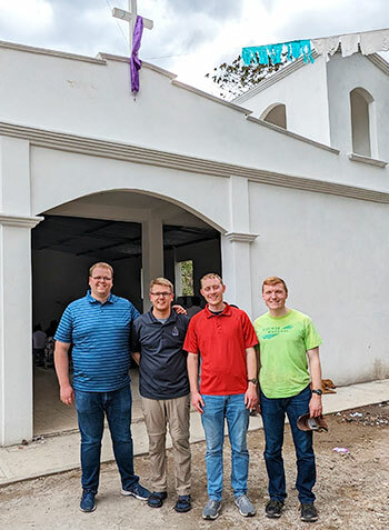 Four smiling men with colorful shirts smile at the camera.