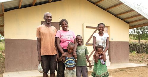 A family smiles while standing in front of their home.