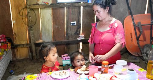 A Guatemalan mother serves rice and beans to her two young children at a table.