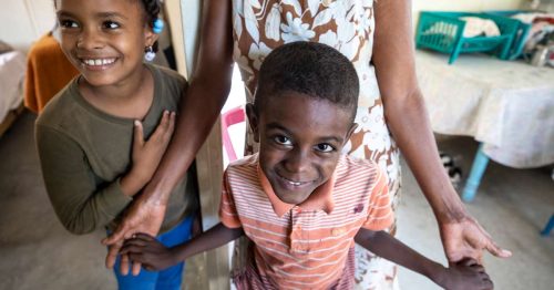 Two young children, a little boy having his hands held.