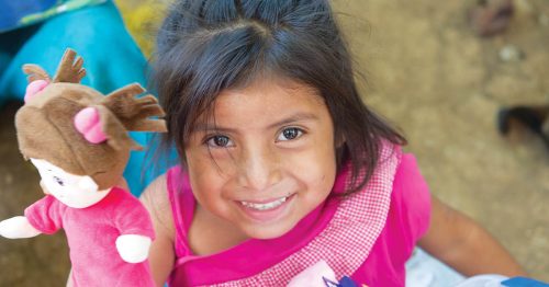 A young Guatemalan girl dressed in pink holds up her brand-new doll.
