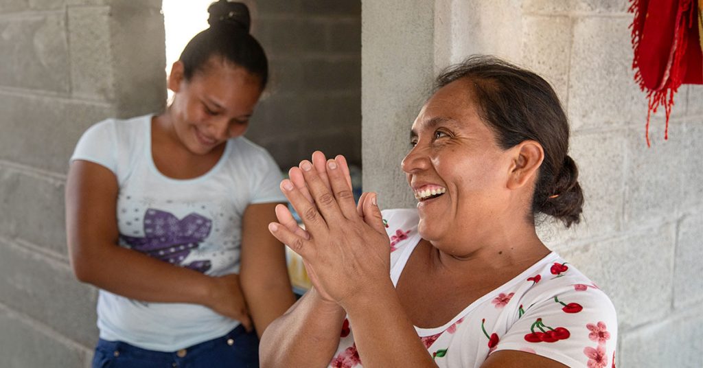 Two women share a laugh as they stand inside a home built of sturdy concrete blocks.