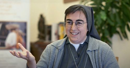 Sister Smerilli smiles at the camera wearing a habit and a gray sweater.