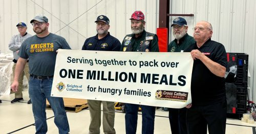 Five men hold a sign that says, “Serving together to pack over one million meals for hungry families.”