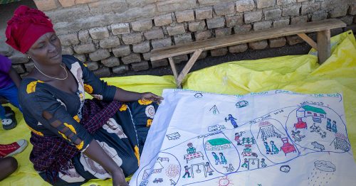 A woman in a red turban holds a sheet of butcher paper with drawings conveying her plans for the future.
