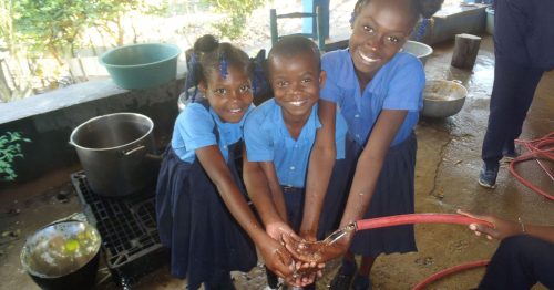 Three schoolchildren wash their hands at a faucet.
