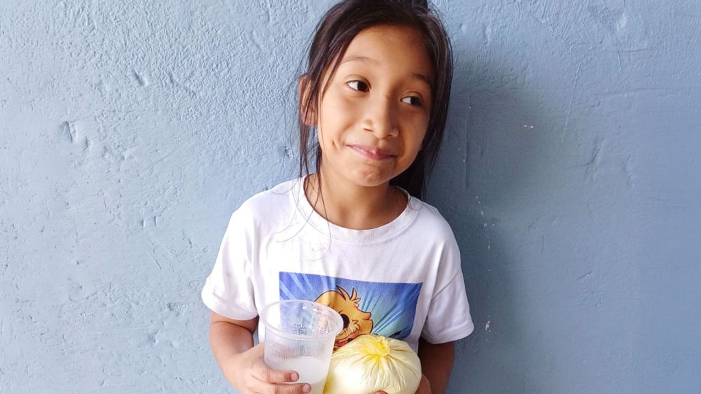 A young girl smiles as she holds a glass of milk.