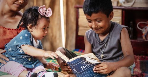 A young boy opens his new bible while his baby sister sits nearby.