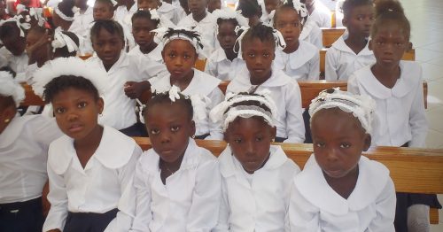 A group of Haitian children all dressed in white and sitting in a chapel.