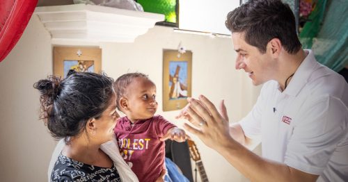 A man interacts with a smiling baby boy held by his mother.