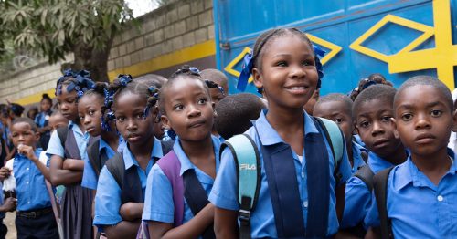 A group of children in Catholic school uniforms stand beside the mission’s front gate.