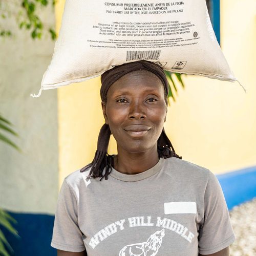 A woman carries a bag of food on her head.