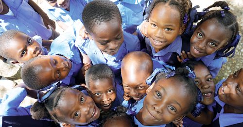 A group of children in school uniforms stands close together, looking up at the camera.