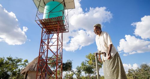 A Catholic sister turns on a water tap with an elevated water tank behind her.