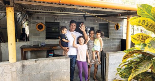 A Guatemalan family waves from their covered front porch.