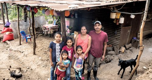 A family stands in front of a home made from mud, sticks and rusted metal.