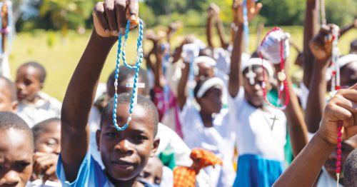A group of children hold up colorful rosaries.