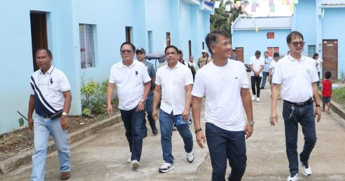 A man smiles broadly as he leads a group of people down a street with new homes.