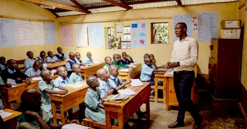 Children at St. John Bosco listen to the teacher at the front of the classroom.