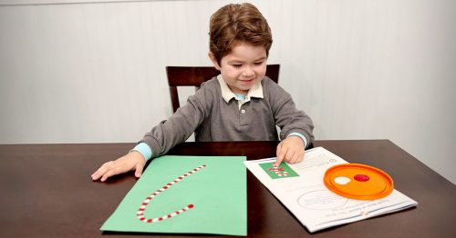 A child fingerpaints a candy cane on green paper.