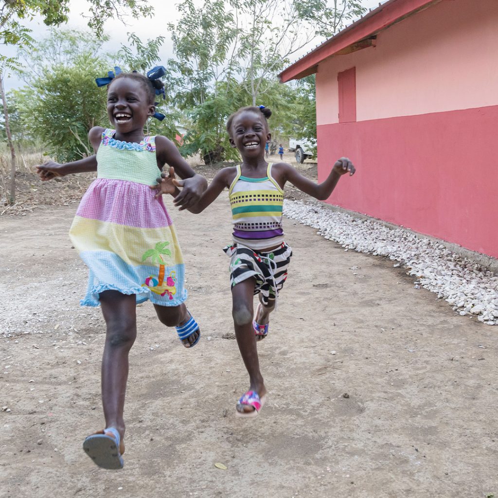 Two young girls run past the side of a new house.