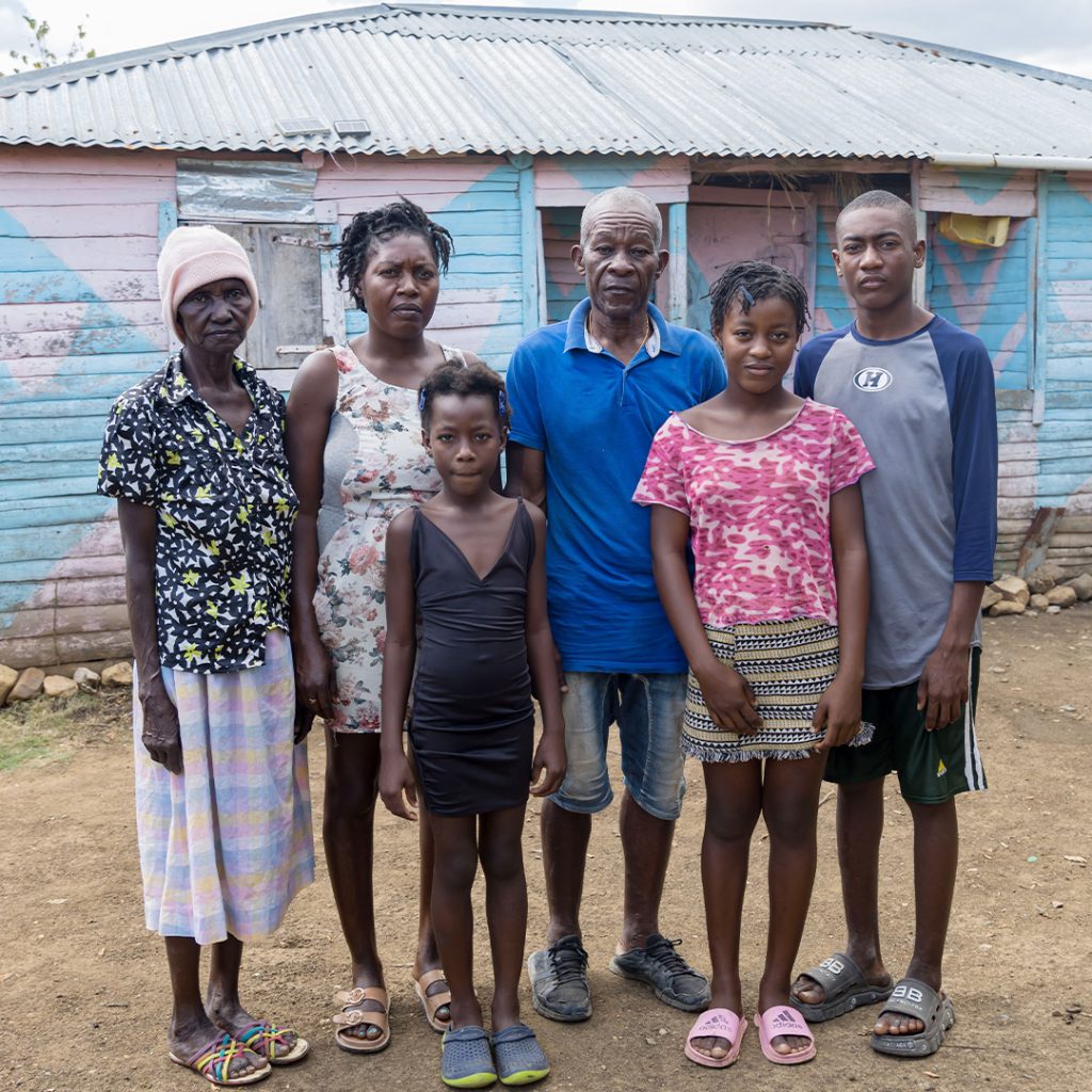 A large family stands in front of a house made of scrap metal.
