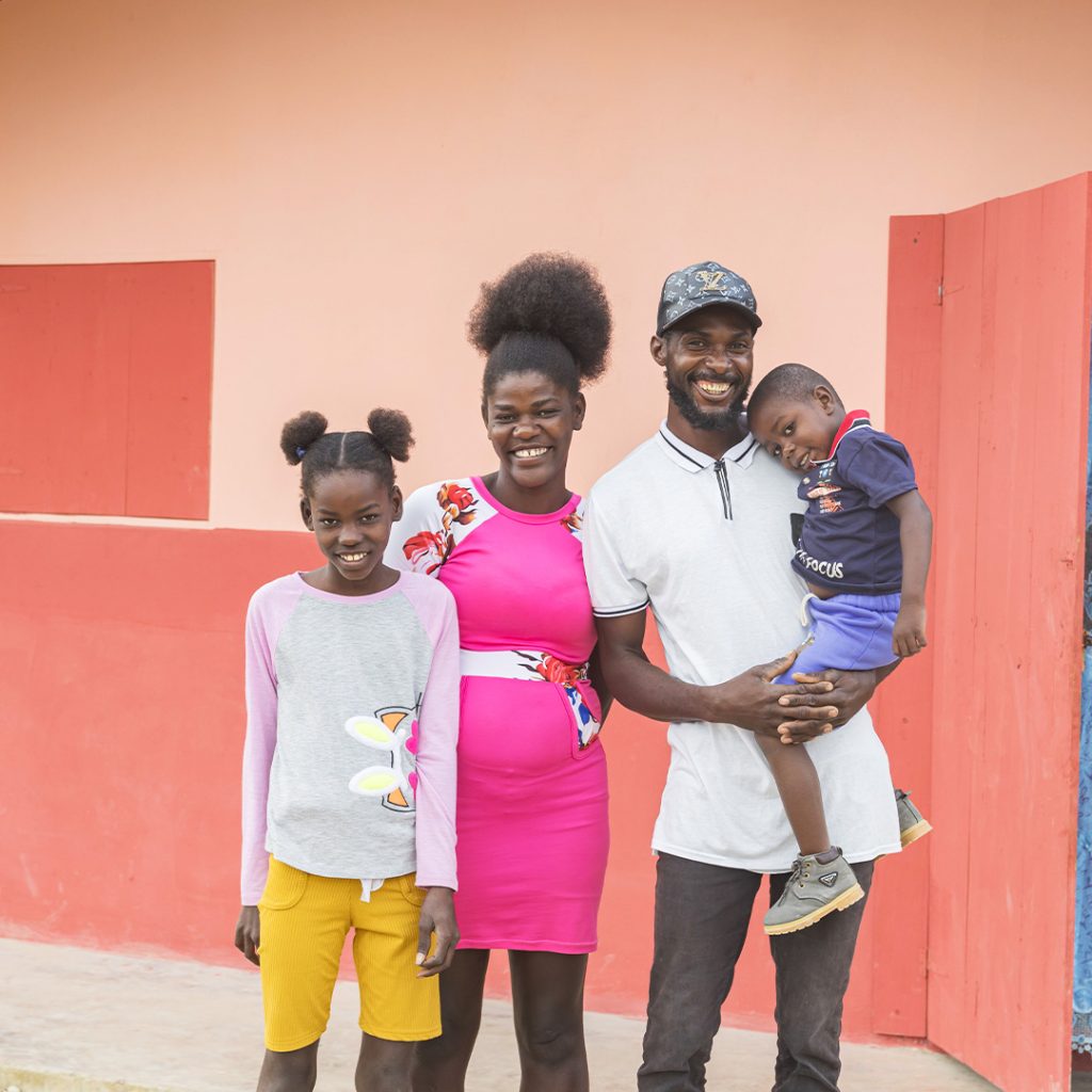 A family with young children smiles in front of a newly constructed home.