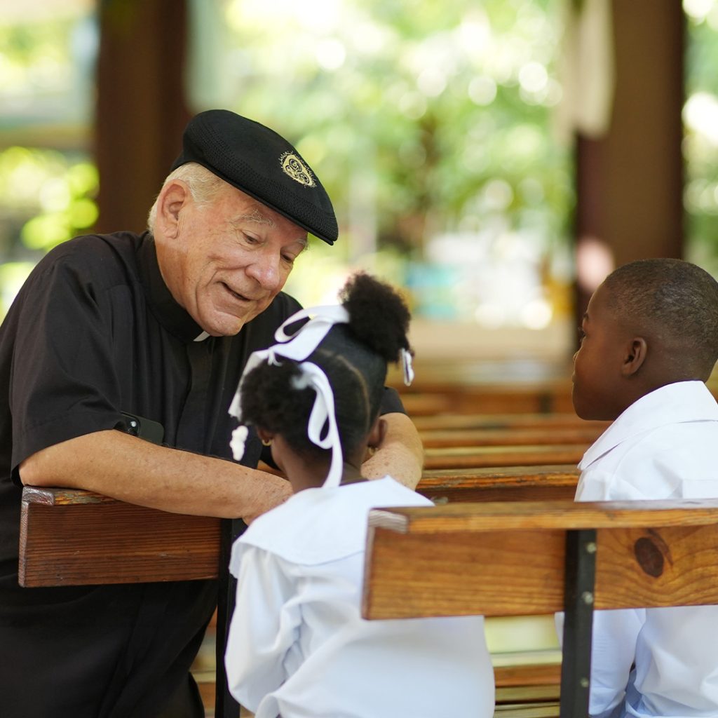 A priest sits with two young children.
