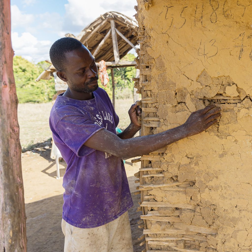 A man points out a crack in the wall of his mud-coated house.