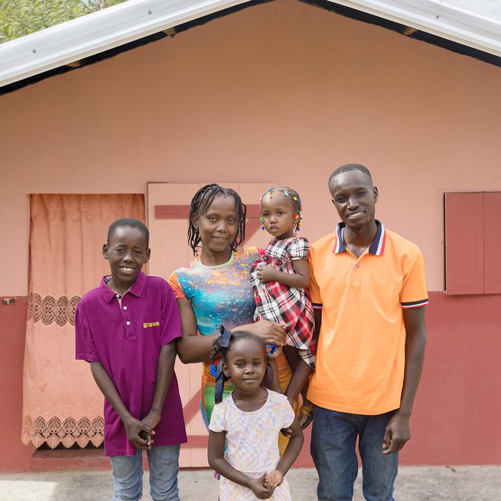 A man and his young family stand in front of a freshly painted new house.