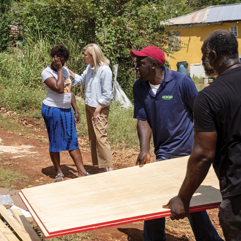 A woman weeps while another speaks to her and touches her shoulder. Men in the foreground of the photo carry lumber.