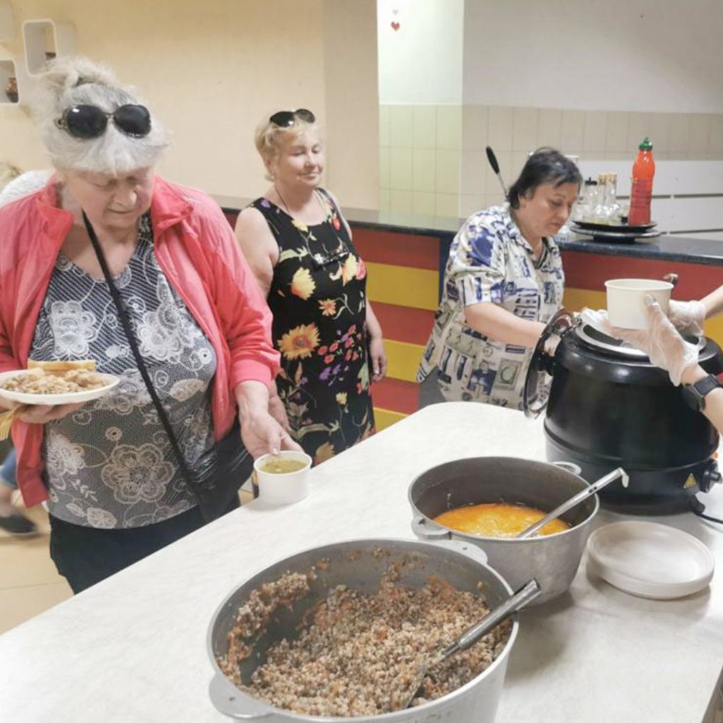Four women serve themselves plates of nutritious food from large pots.