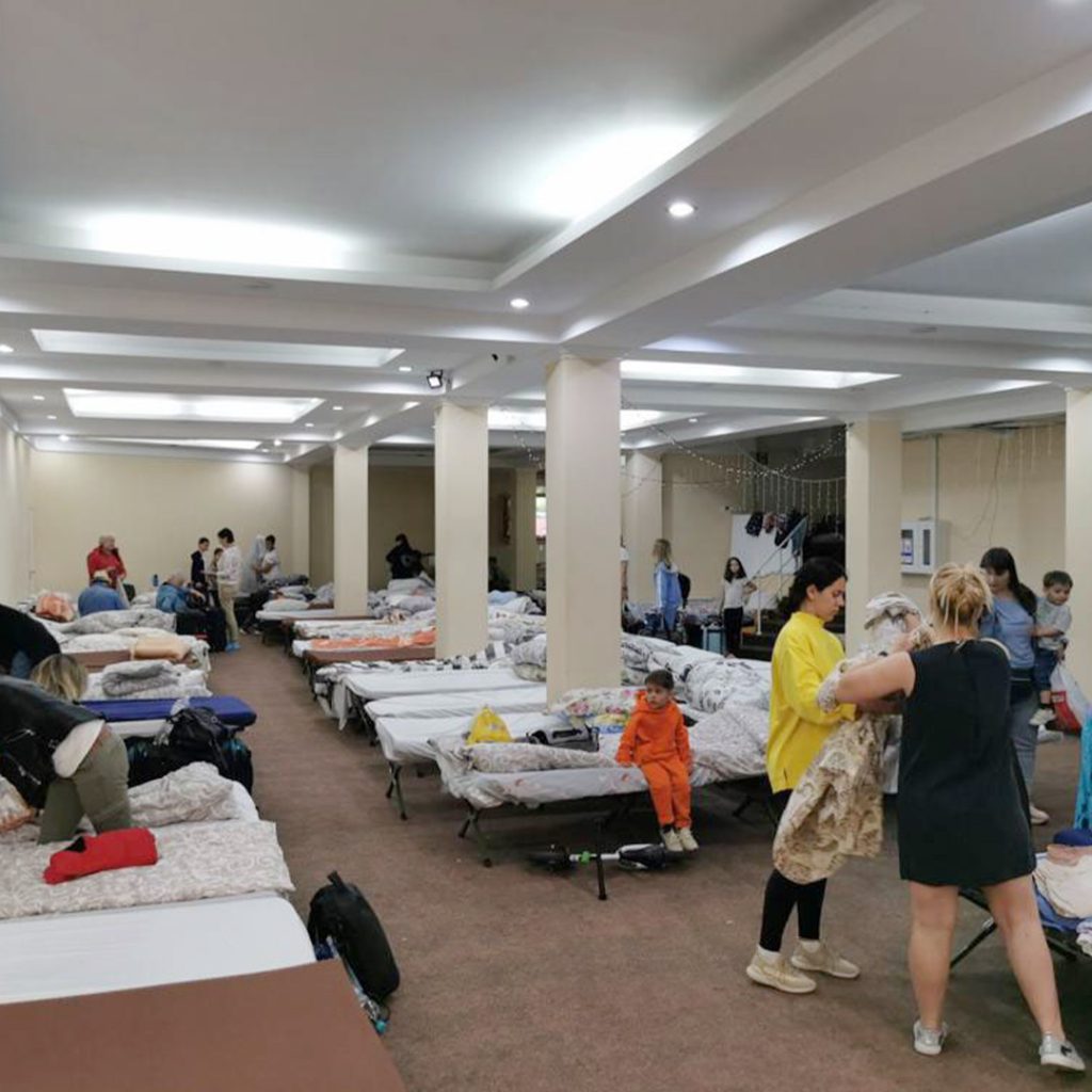Adults and children in a room with lines of clean beds.