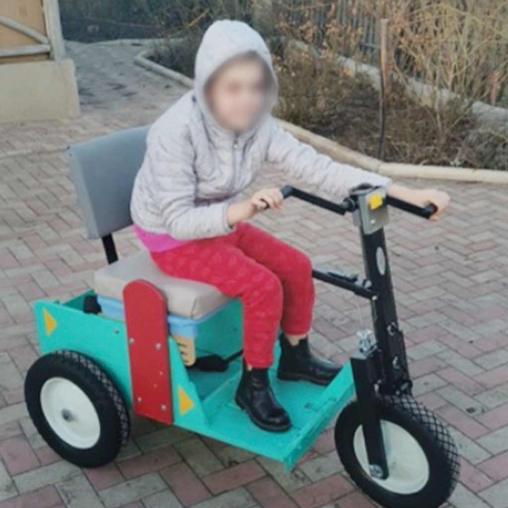A girl rides on a teal mobility cart with three wheels.