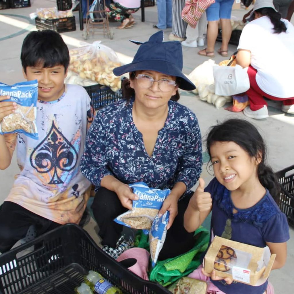 A woman and two children hold up items from a food distribution basket.
