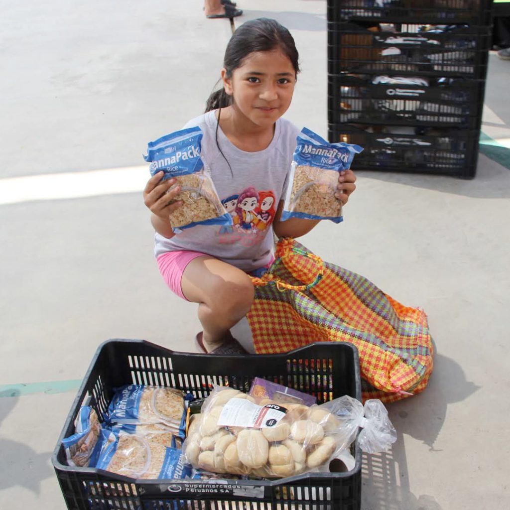 A young girl kneeling next to a small crate of food items holds up two Vitafood meal packs.