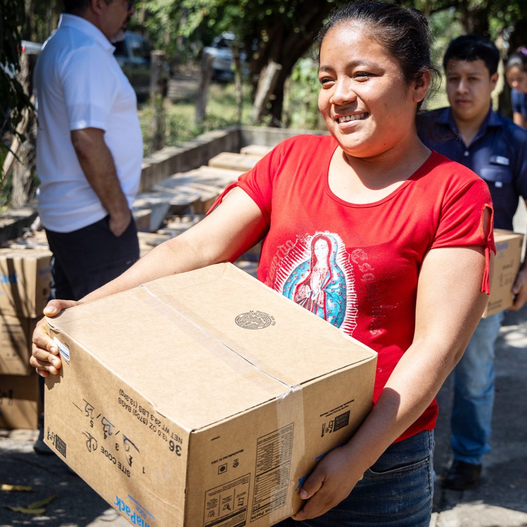 Vitafood recipients carry cases of food packs at a distribution event.