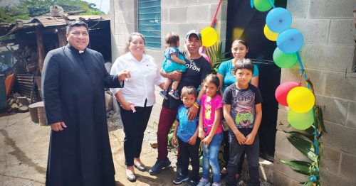 A priest presents house keys to a family standing in the doorway of a home.