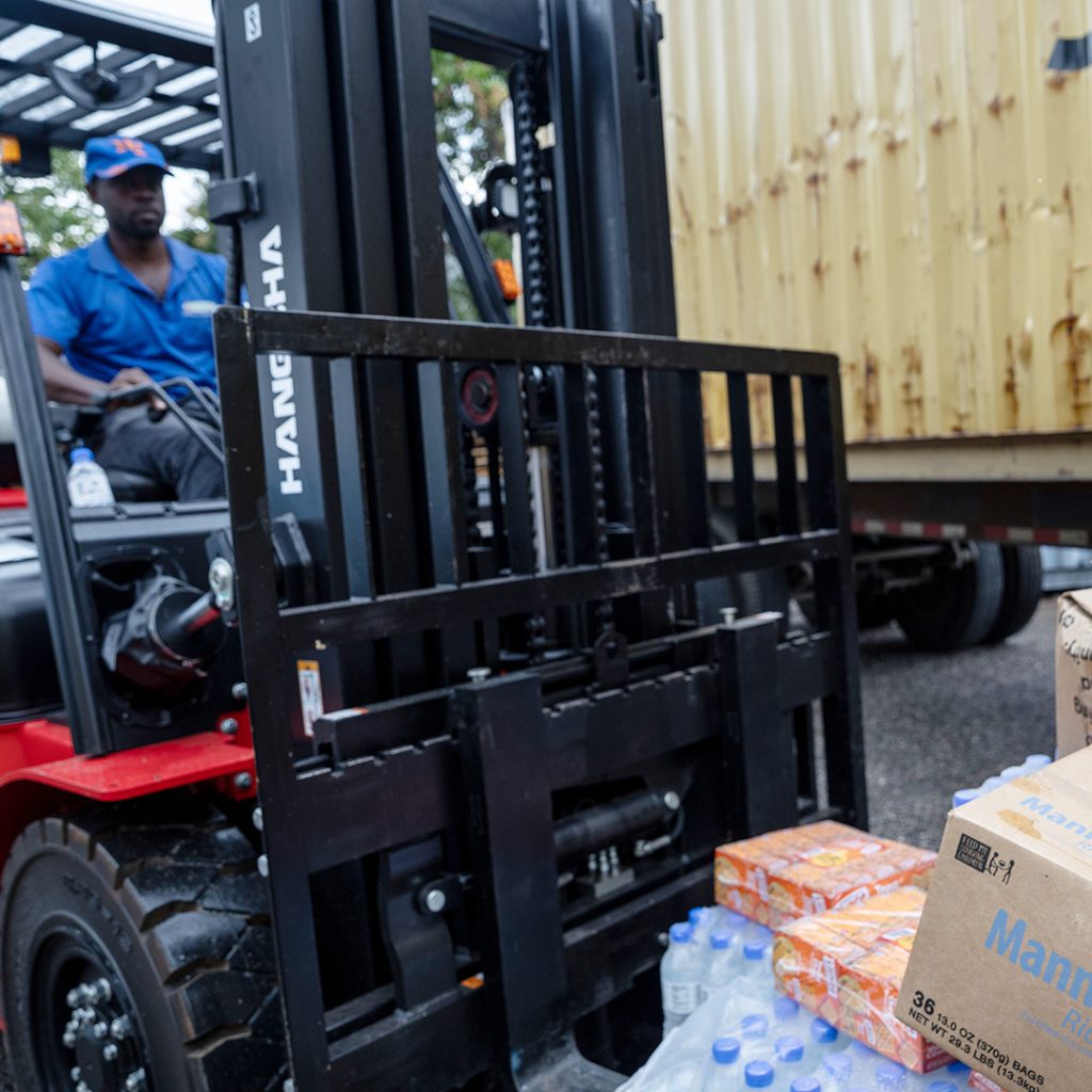 A man on a forklift transports a pallet of bottled water and food.