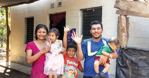 A Guatemalan family waves from their covered front porch.