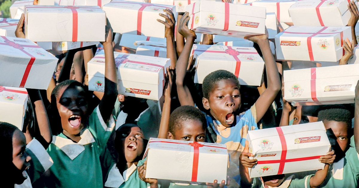 Un grupo de estudiantes de primaria levanta sus regalos de Box of Joy® mientras celebra con alegría.