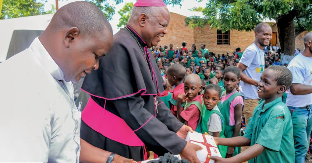 El obispo Mtumbuka entrega un regalo de Box of Joy a un niño que lleva el uniforme del colegio.