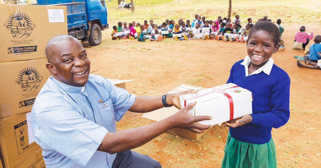 Una estudiante de primaria sonríe mientras recibe un regalo de Box of Joy del padre Steven.