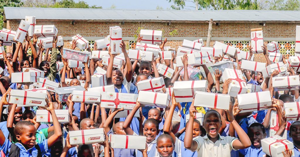 Un grupo de estudiantes de primaria celebra con alegría mientras sostiene regalos de Box of Joy.