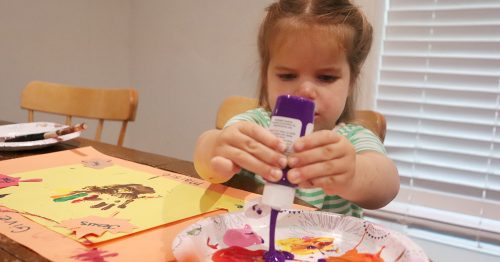 A little girl squeezes paint while making a Thanksgiving placemat.