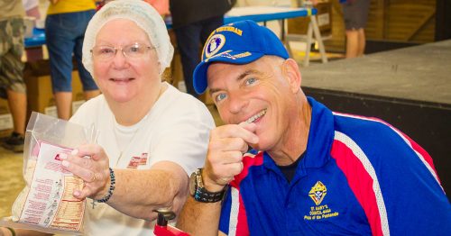A smiling man sits next to a woman holding up a bag.
